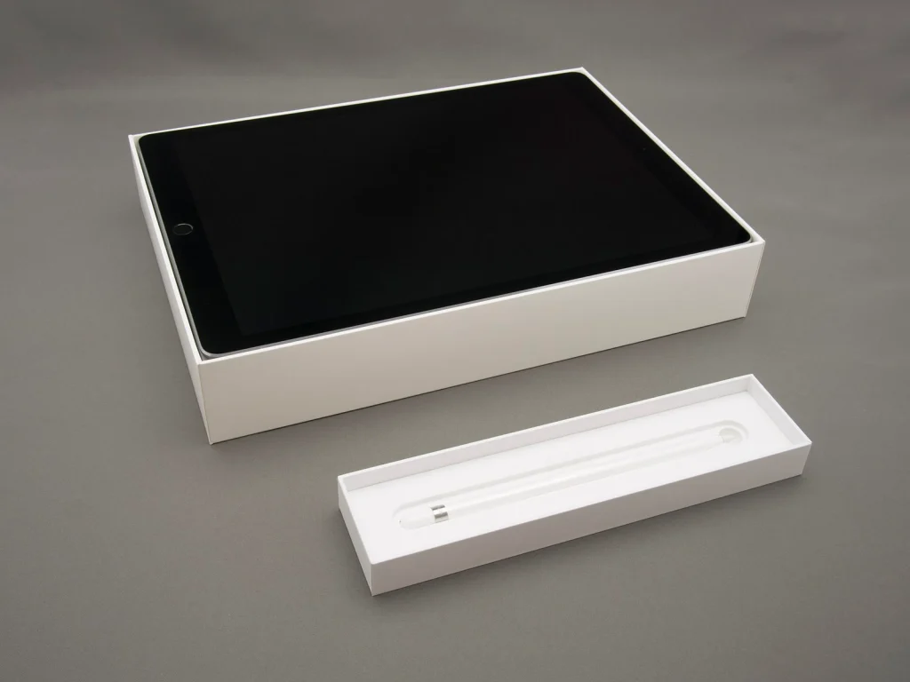 회색 바닥 위 개봉한 상자에 담긴 iPad Pro와 별도 트레이의 Apple Pencil